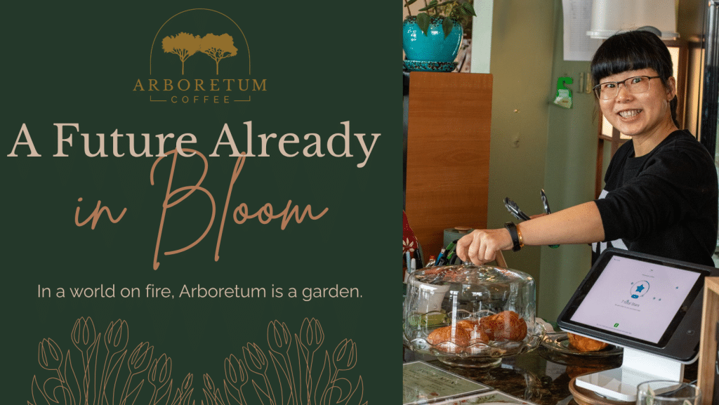A barista smiling while preparing coffee behind a counter at Arboretum Coffee. Displayed items include pastries under a glass cover, accompanied by a tablet for orders.